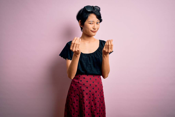 Junge schöne asiatische Mädchen in lässigem Kleid vor isoliertem rosa Hintergrund stehend Geld Geste mit den Händen zu tun, um Gehaltszahlungen zu fordern, Millionärsgeschäft - Foto, Bild