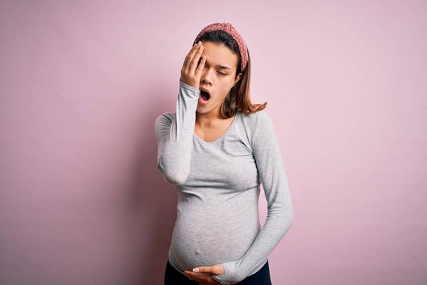 Mladý krásný teenager dívka těhotná očekává dítě přes izolované růžové pozadí Zívání unavený pokrývající polovinu obličeje, oko a ústa s rukou. Tvář bolí bolestí. - Fotografie, Obrázek