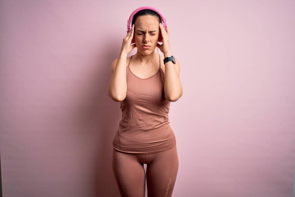 スポーツワークアウトの服を着て若いフィットネス女性は、痛みや片頭痛のために必死の頭痛やストレスに苦しんで音楽に耳を傾けヘッドフォンを着用。手を頭に. - 写真・画像
