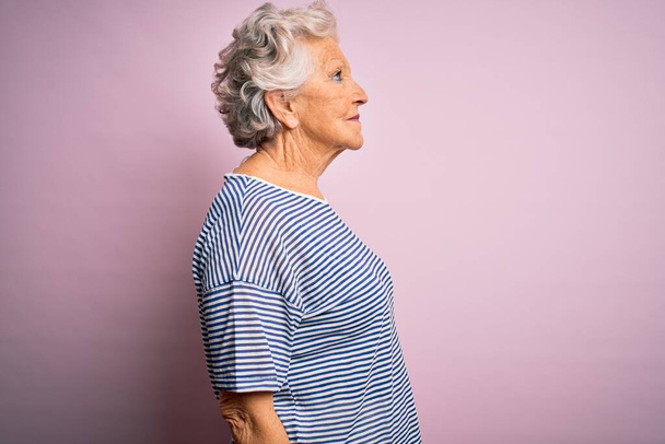 Старша красива сіро-волохата жінка в повсякденній футболці над ізольованим рожевим тлом, дивлячись в бік, розслабляє профільну позу з природним обличчям з впевненою посмішкою
. - Фото, зображення