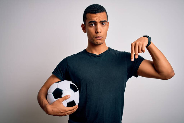 Handsome african american man playing footbal holding soccer ball over white background Pointing down looking sad and upset, indicating direction with fingers, unhappy and depressed. - Photo, Image