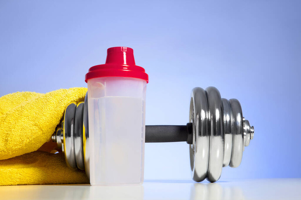Dumbbell and whey protein shaker on a blue towel surface. Sports bodybuilding supplements or nutrition. Fitness or healthy lifestyle concept. - Foto, Imagen