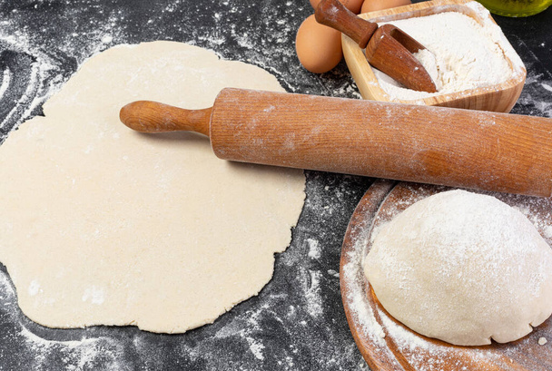 Preparation of the dough. The rolling pin with flour on a dark background. - Φωτογραφία, εικόνα