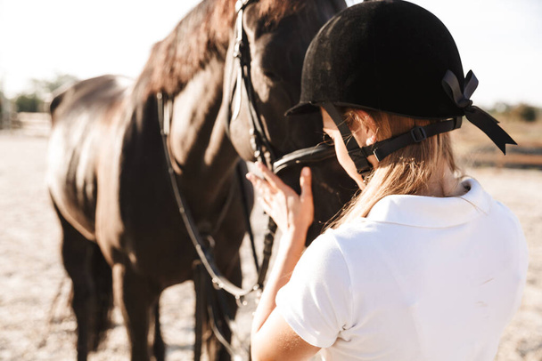 Image of serious amazing young blonde beautiful woman wearing hat with horse in countryside outdoors - Foto, Bild