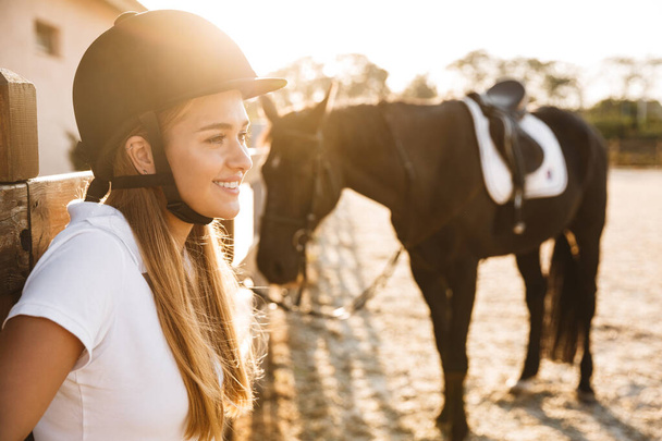 Image of smiling happy young beautiful woman wearing hat with horse in countryside outdoors - 写真・画像