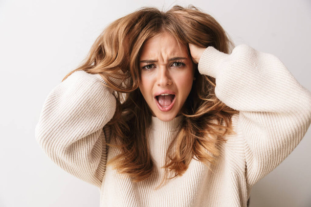 Image closeup of young woman wearing sweater screaming and grabbing her head isolated over white background - Φωτογραφία, εικόνα