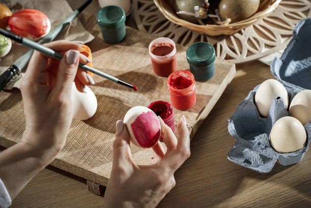 Female hands painting Easter eggs on wooden table on a spring day. Easter decoration time.Colorful eggs and paints on wooden board. - Foto, Imagem