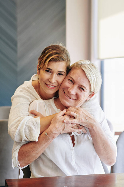 Portrait of smiling young pretty woman hugging her senior happy mother from behind - Photo, image