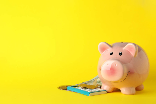 Piggy bank, money and calculator on yellow background, space for text - Foto, afbeelding
