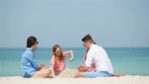 Familia de cuatro haciendo castillo de arena en la playa tropical blanca
 - Metraje, vídeo