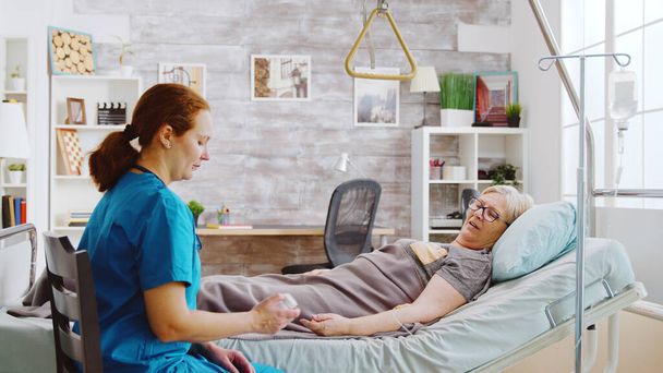 Valkoihoinen sairaanhoitaja näyttää vanhalle naiselle pillereiden annoksen, jonka hänen pitäisi ottaa
 - Valokuva, kuva