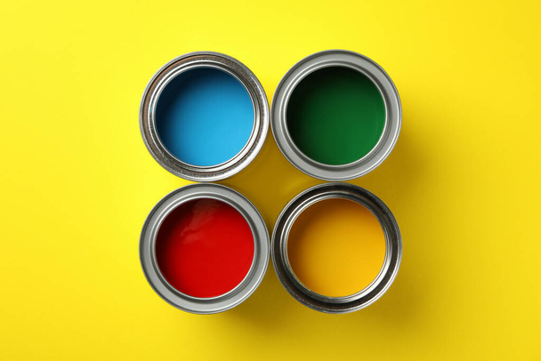 Cans with different paint on yellow background, top view - Foto, immagini