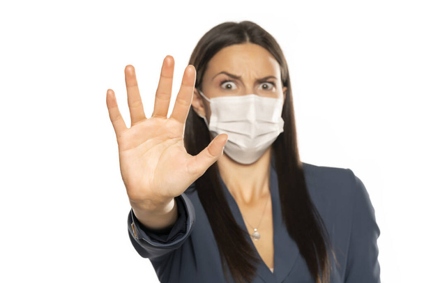 Mujer enojada con mano parada y máscara protectora en su cara sobre fondo blanco
 - Foto, imagen