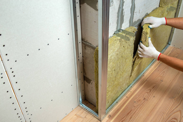 Працівник утеплює стіну кімнати теплоізоляцією з мінеральної вати
. - Фото, зображення