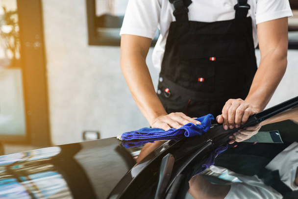 Bir adam arabayı temizliyor ve kuru mavi bir mikrofiber havlu ile bir çizik çıkarıyor, araba temizleme (veya valelik) konsepti. Otomobil profesyonel temizlik servisi. Seçici odak. - Fotoğraf, Görsel