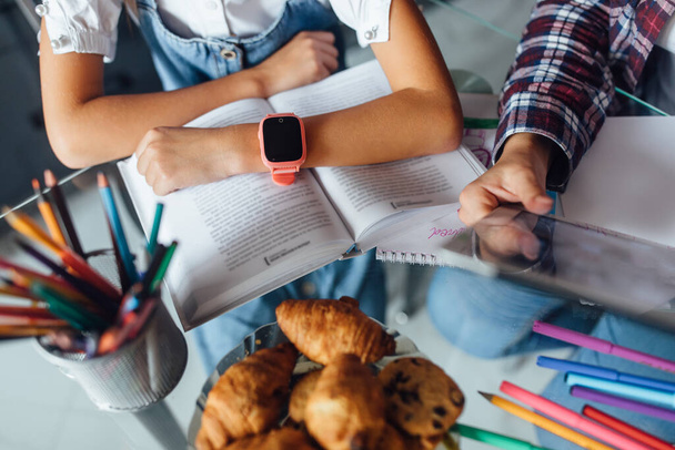 Children hands doing homework with mom, close up photo, pink smart watches at kid hand. - Фото, зображення