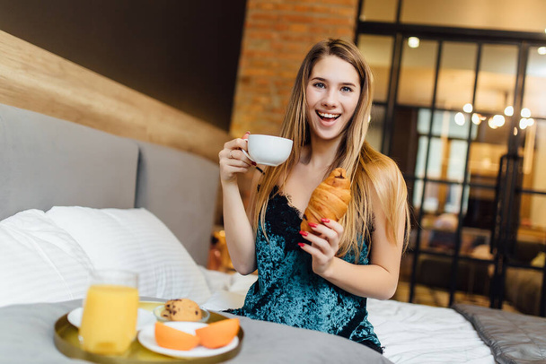 Portrait of a happy woman have a breakfast on bedroom with fresh orange juice and croissant. - Valokuva, kuva