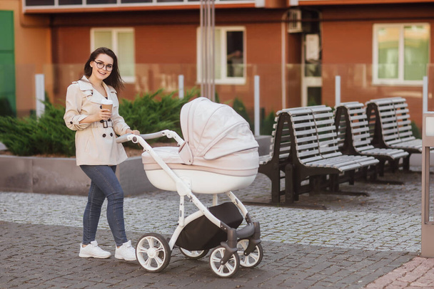Woman walk with stroller and coffee. Fashion girl, mom with pram. Mother with child. - Fotoğraf, Görsel