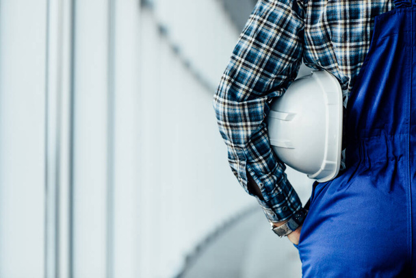 Close up back view of male construction worker holding helmet intdoor. - Fotó, kép