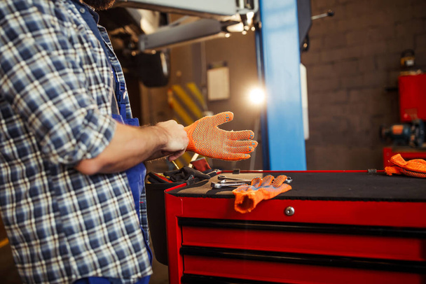 male mechanic putting on gloves for a work in garage, cropped shot - Foto, Imagem