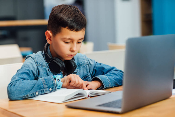 Portrait of concentrated boy with laptop doing homework and writing. - Photo, image