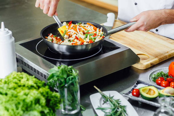 Close up photo, man hands with apron frying vegetables, modern kitchen. - Foto, Bild