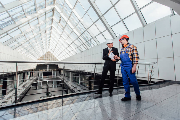 Business male or entrepreneur in helmet discussing new project with foreman and holding blueprint in corridor. - 写真・画像