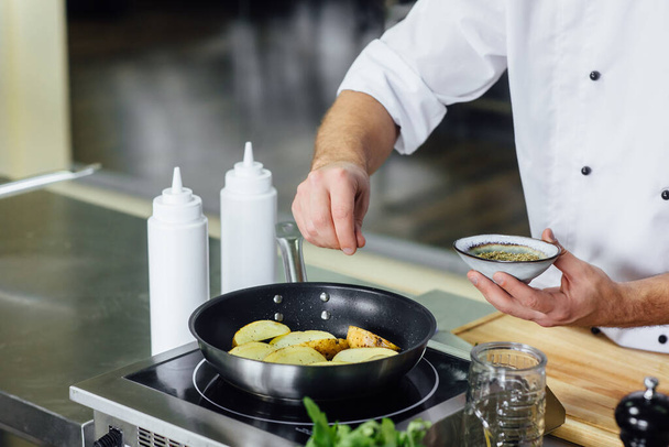Male chef cooking fresh potato, sauce in restaurant kitchen. Cook at work during dinner service. Italian style cuisine, lifestyle and healthy food concept. Focus on his hand. - Foto, Imagem