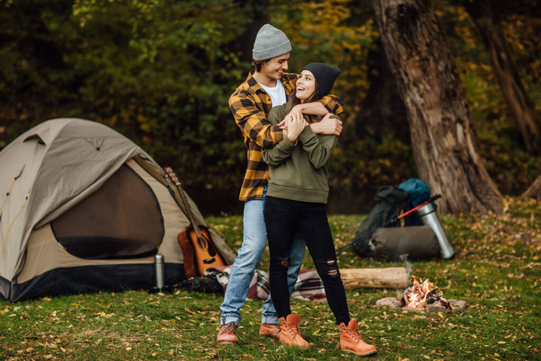 Feliz casal amoroso de turista em roupas casuais na floresta perto da tenda. Um homem bonito abraça uma mulher atraente
. - Foto, Imagem