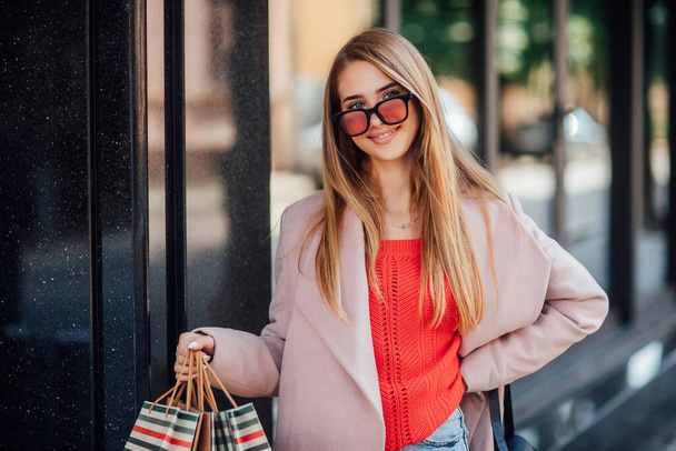 Bir genç gülümseyen kız başarılı bir alışveriş torbaları ile sokakta yürürken elinde sahiptir. - Fotoğraf, Görsel