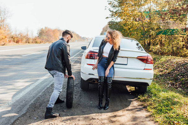 Man changing tire that are leaking his car broke down at woman car. - Fotoğraf, Görsel