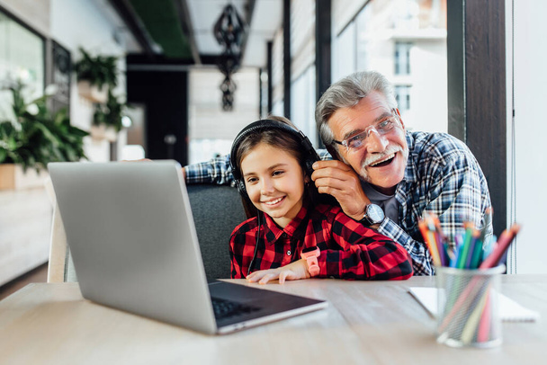 Funny old man with his granddaughter using laptop for play game with headphones. - Фото, зображення