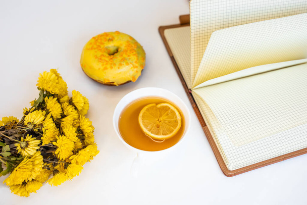 Tea with lemon and flowers on a white background. Workpiece with notepad and donut - Foto, afbeelding