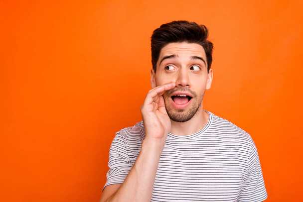 Close up photo of funky silly macho guy chatterbox hold arm near mouth telling secrets wear casual striped t-shirt isolated over bright orange color background - Foto, Bild