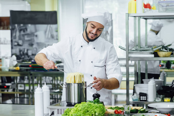 Bärtiger, professioneller Chefkoch in weißer Uniform, kocht Spahhetti, Küchengeräte. - Foto, Bild