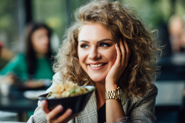 Blonde girl with long hair in a restaurant on ship. Girl tries salmon with rice. Girl eats appliances. The girl in the jacket after work eats. - Фото, изображение