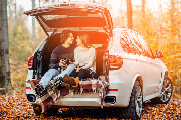 Beautiful pretty couple enjoying picnic time on the forest. They drinking tea and sitting in a car. - Fotoğraf, Görsel