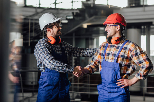 Two young builders in working uniform and helmets ready for a work, handshake. - Foto, afbeelding