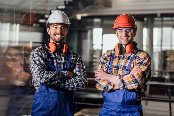 Two young builders in working uniform and helmets crossed arms. - Fotó, kép