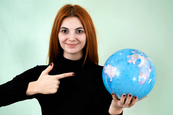 Portrait of a happy young woman holding geographic globe of the world in her hands. Travel destination and planet protection concept. - Fotó, kép