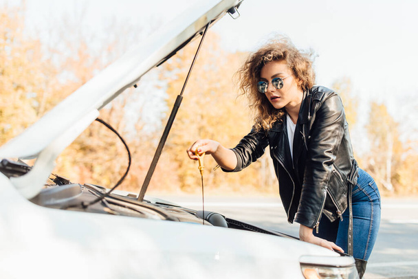 Young woman driver standing near broked car with open hood. - 写真・画像
