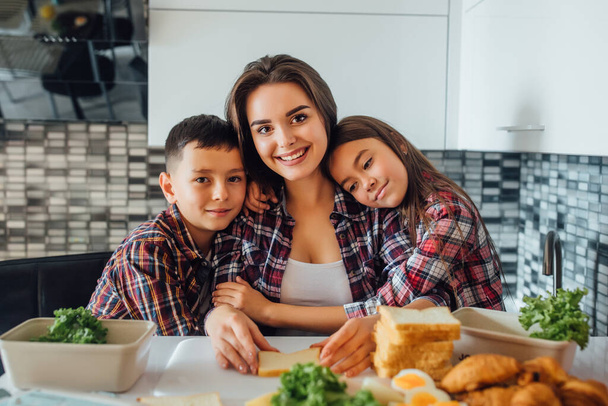 Junge schöne Mutter mit ihren Kindern, die sich während des Frühstücks in der Küche umarmen. - Foto, Bild