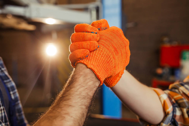 close up of mechanics shaking hands in the gloves in the garage, sun effect - Zdjęcie, obraz