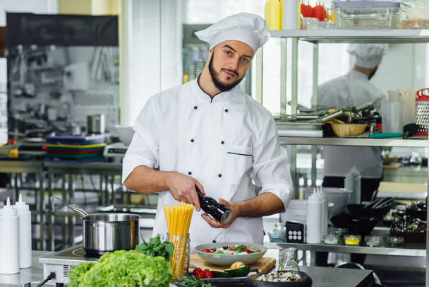 Профессиональный повар-мужчина веселится и радуется на профессиональной кухне, готовит салат и спагетти
. - Фото, изображение