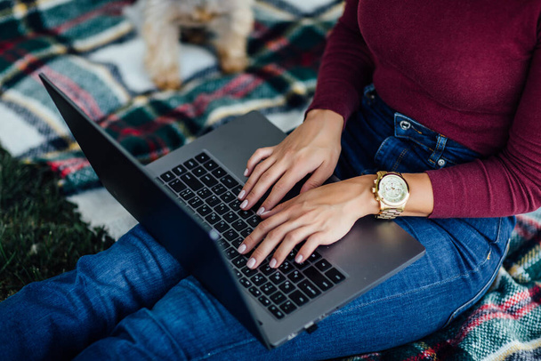 De cerca foto, estudiante mujer sentada en la manta y tener un tiempo de picnic con su ordenador portátil y Yorkshire terrier perro
. - Foto, imagen