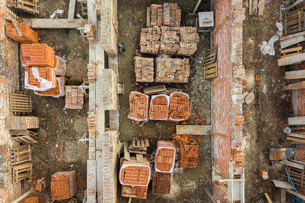 Letecký pohled na staveniště pro budoucí zděný dům, betonovou podlahu a hromady žlutých hliněných cihel pro stavbu. - Fotografie, Obrázek