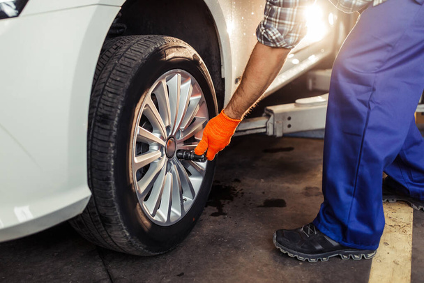 Close up shot of auto mechanic changing tire in workshop - Photo, image