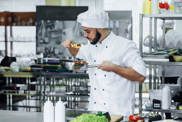 Happy successful young chef in white uniform preparing a meal with various vegetables. - Foto, Imagen