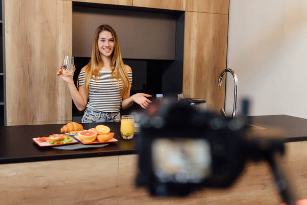 Pretty young blonde woman blogger drinking water in kitchen with healthy food on table. Healthy food time. - Fotoğraf, Görsel