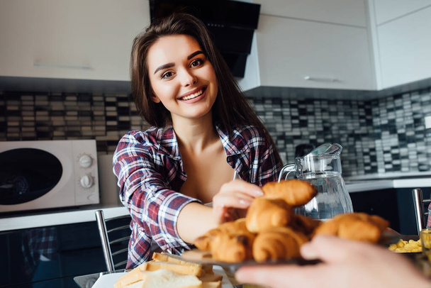Portrait of young cheerful woman holding fresh croissant on hands and smiling. - Foto, imagen